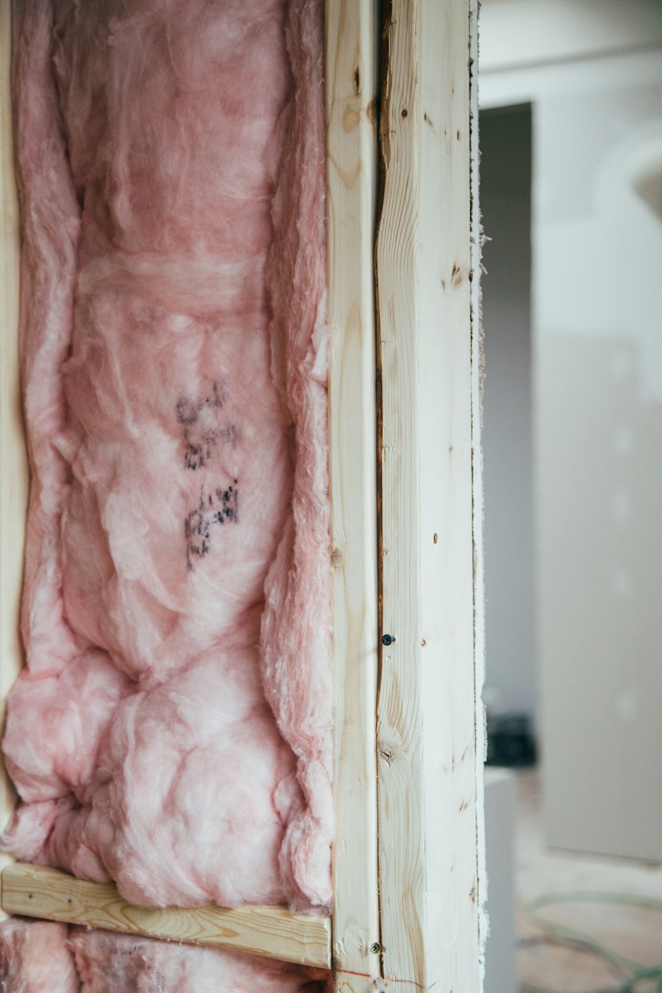 Rosa Glasfaserisolierung füllt Holzständer in einer Wand während des Baus.